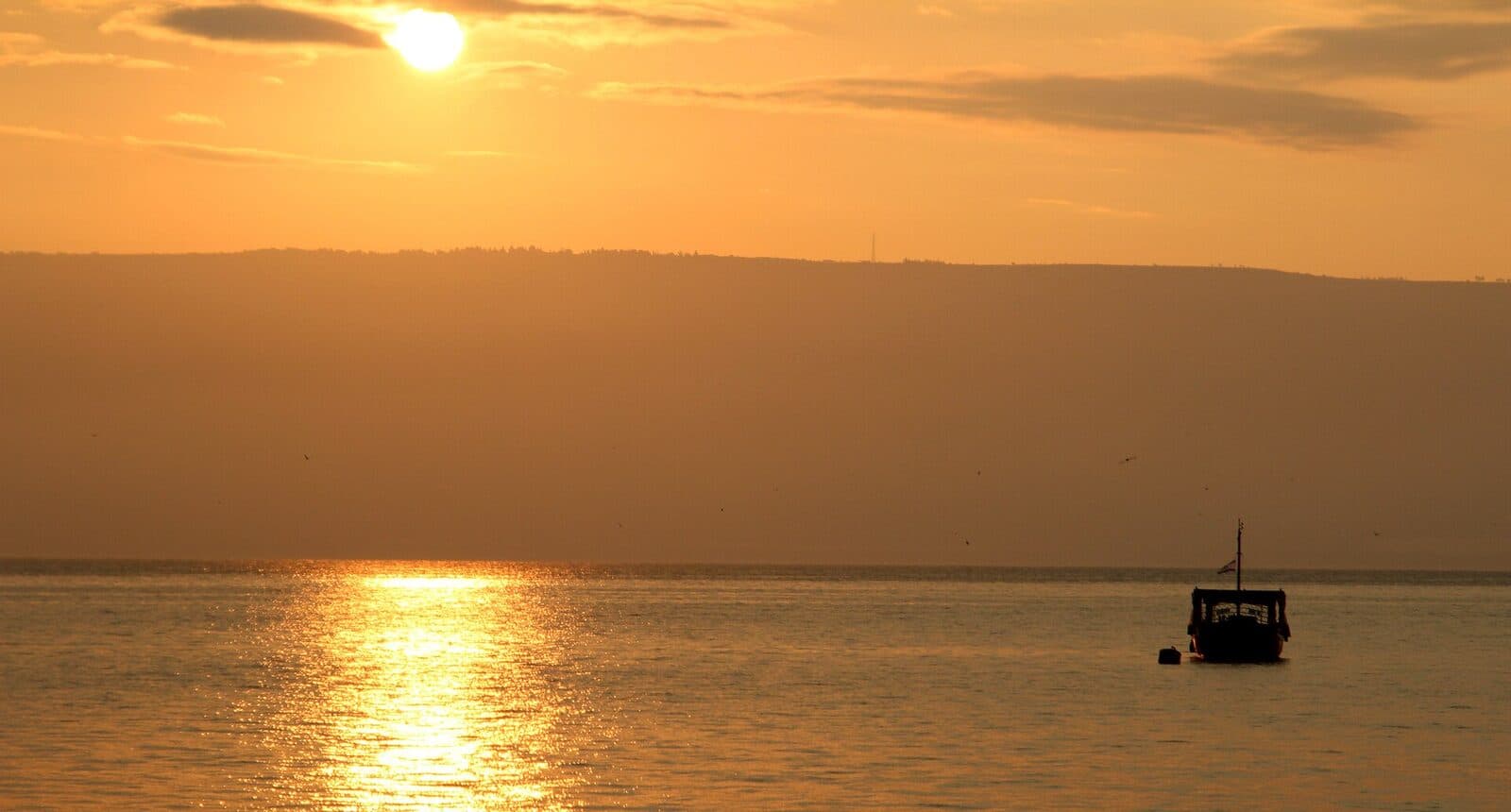 Sunrise over the Sea of Galilee, with a lone wooden boat on the water