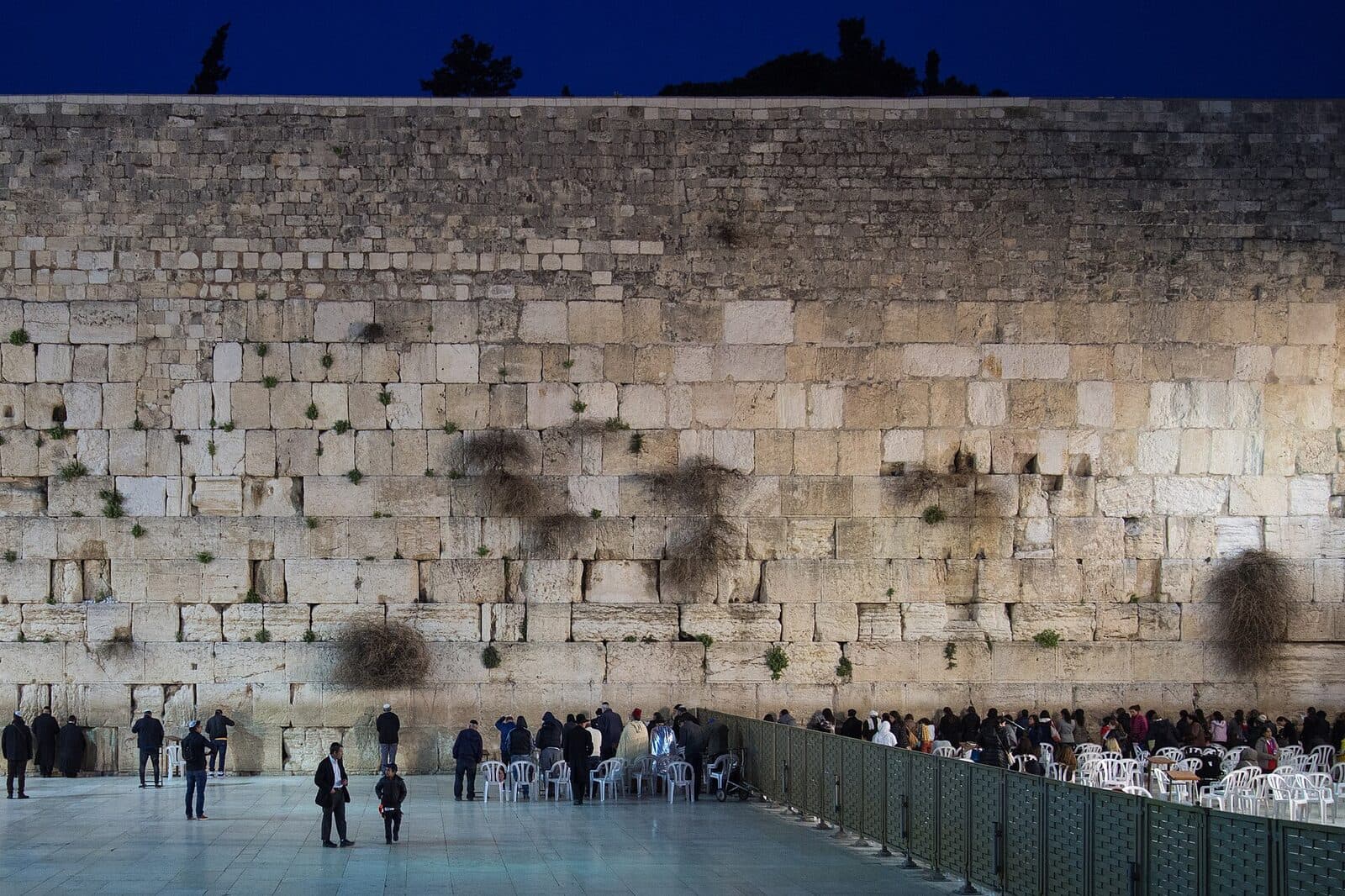 The Western Wall softly lit at dusk, with worshippers gathered at its foot